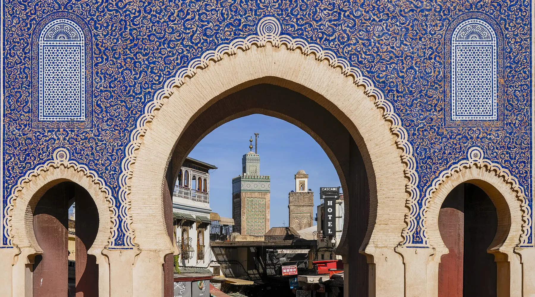 The Bab Bou Jeloud gate in Fes, covered in blue zellij tile, framing the minaret of the Bou Inania Madrasa.